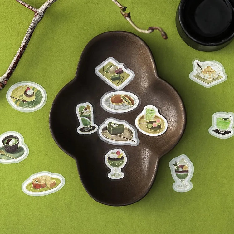 Green matcha-themed café flake sticker sheet with illustrated desserts, tea bowls and small plates accented with foil.