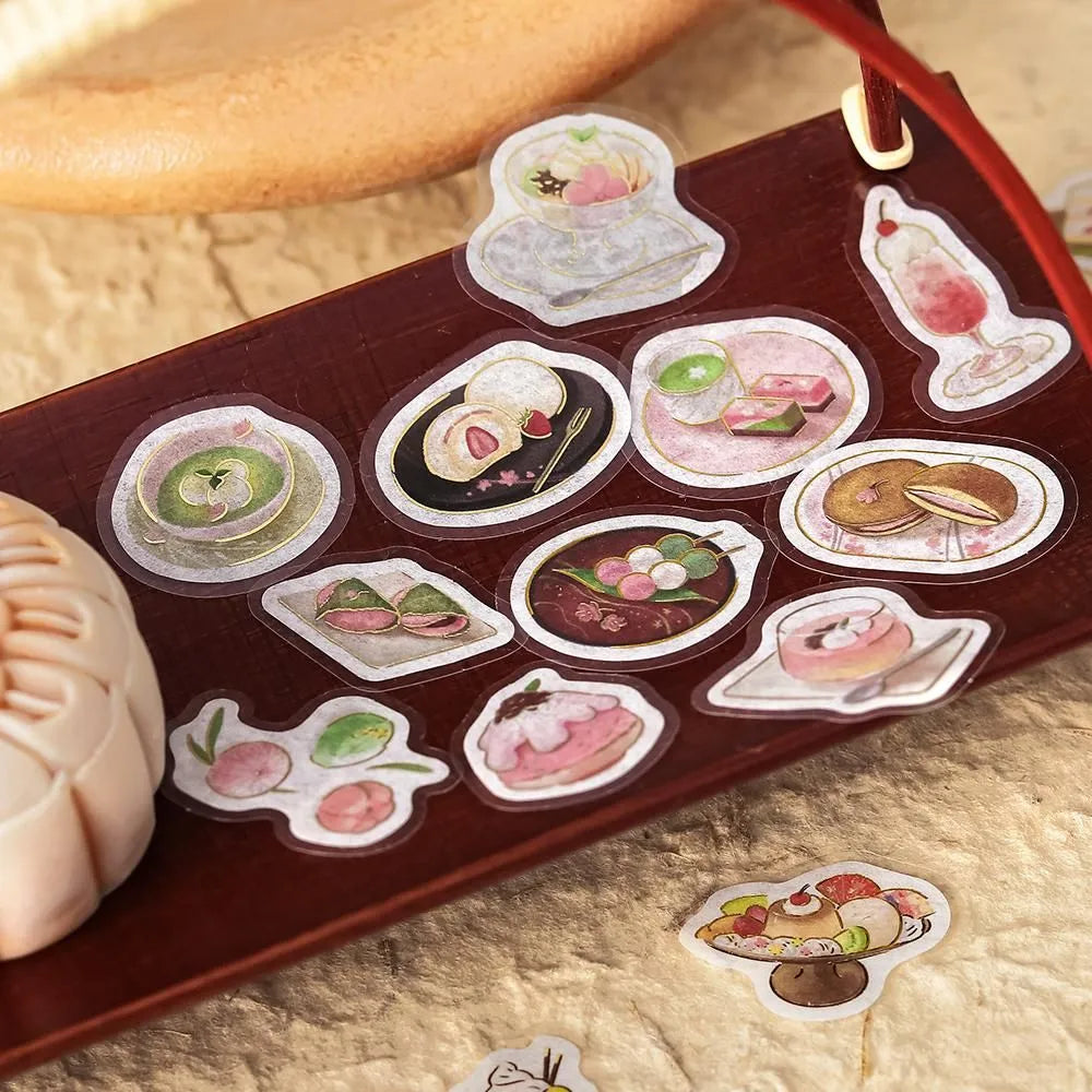 Pink-toned café flake stickers showing cakes, parfaits and delicate desserts with warm foil accents on washi paper.