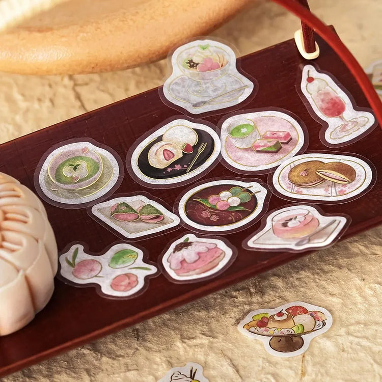 Pink-toned café flake stickers showing cakes, parfaits and delicate desserts with warm foil accents on washi paper.