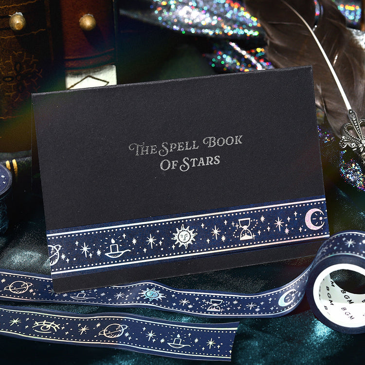 A roll of BGM washi tape in deep midnight blue featuring celestial motifs—sun, moon, hourglass, and stars—accented with shimmering foil from the Grimoire of Stars collection.