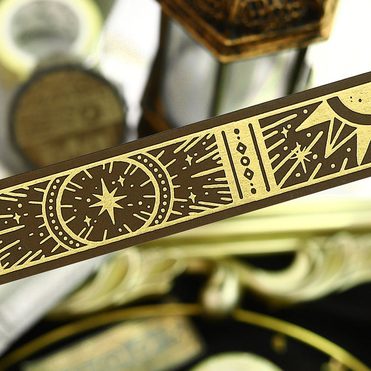 A roll of gold-toned washi tape with celestial suns, moons, and foil accents from the Grimoire of Stars Holy edition.