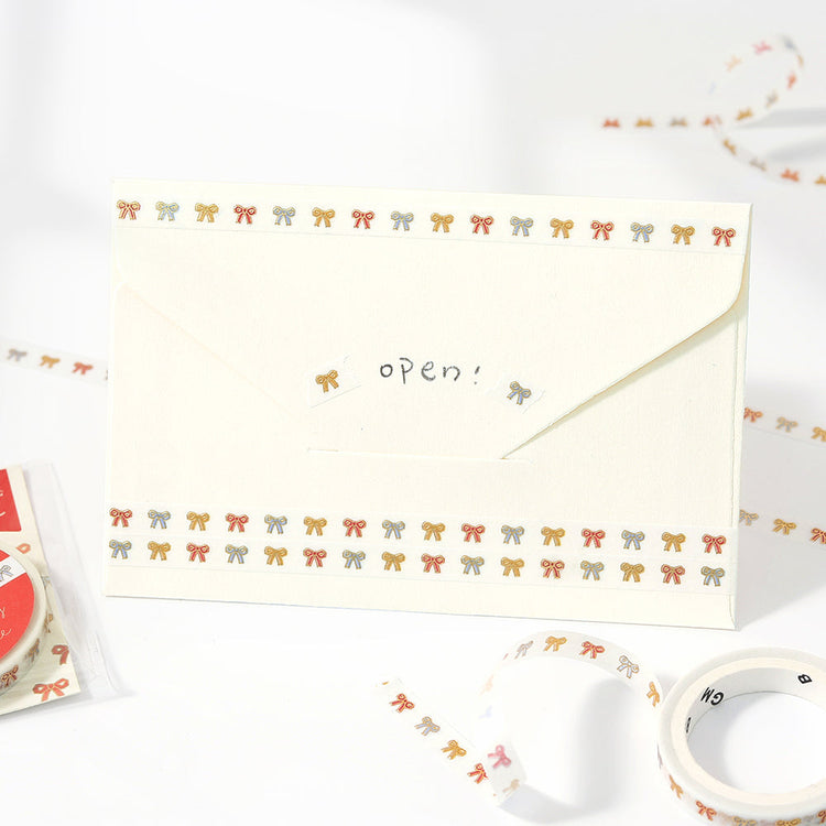 A roll of washi tape decorated with cute ribbon patterns highlighted by metallic foil, adding a playful and sparkling detail to journals, planners, and craft projects.