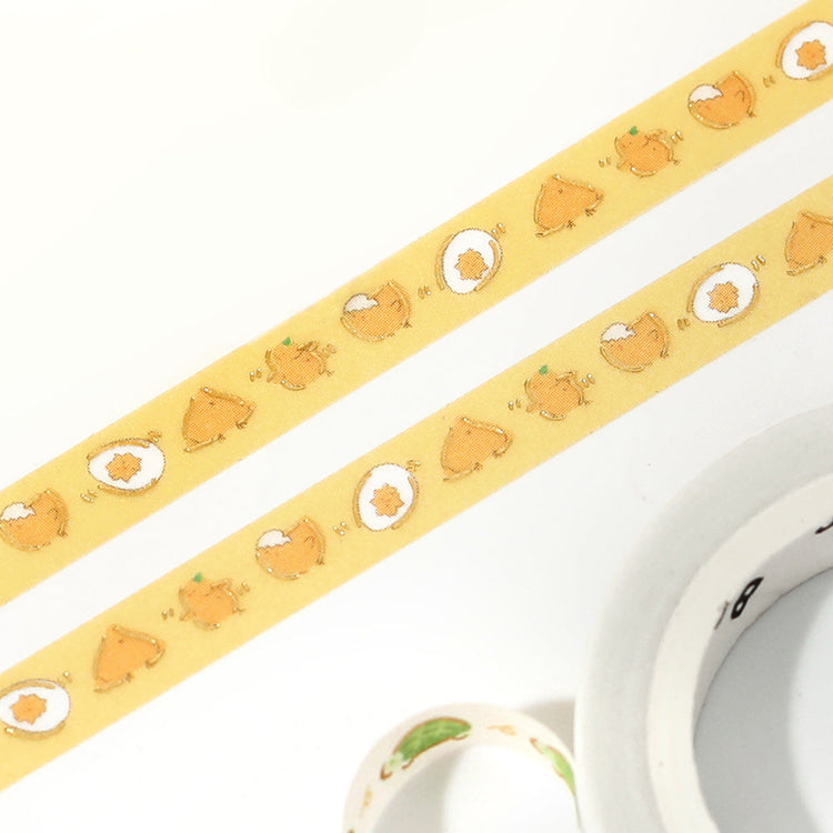 A slim roll of washi tape featuring a repeating design of playful yellow chicks running, accented with metallic foil highlights—perfect for planners, journaling, and decorative crafts.
