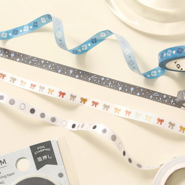 A slim 5mm washi tape roll with star patterns highlighted in metallic foil, designed for journaling, scrapbooking, and decorative accents.
