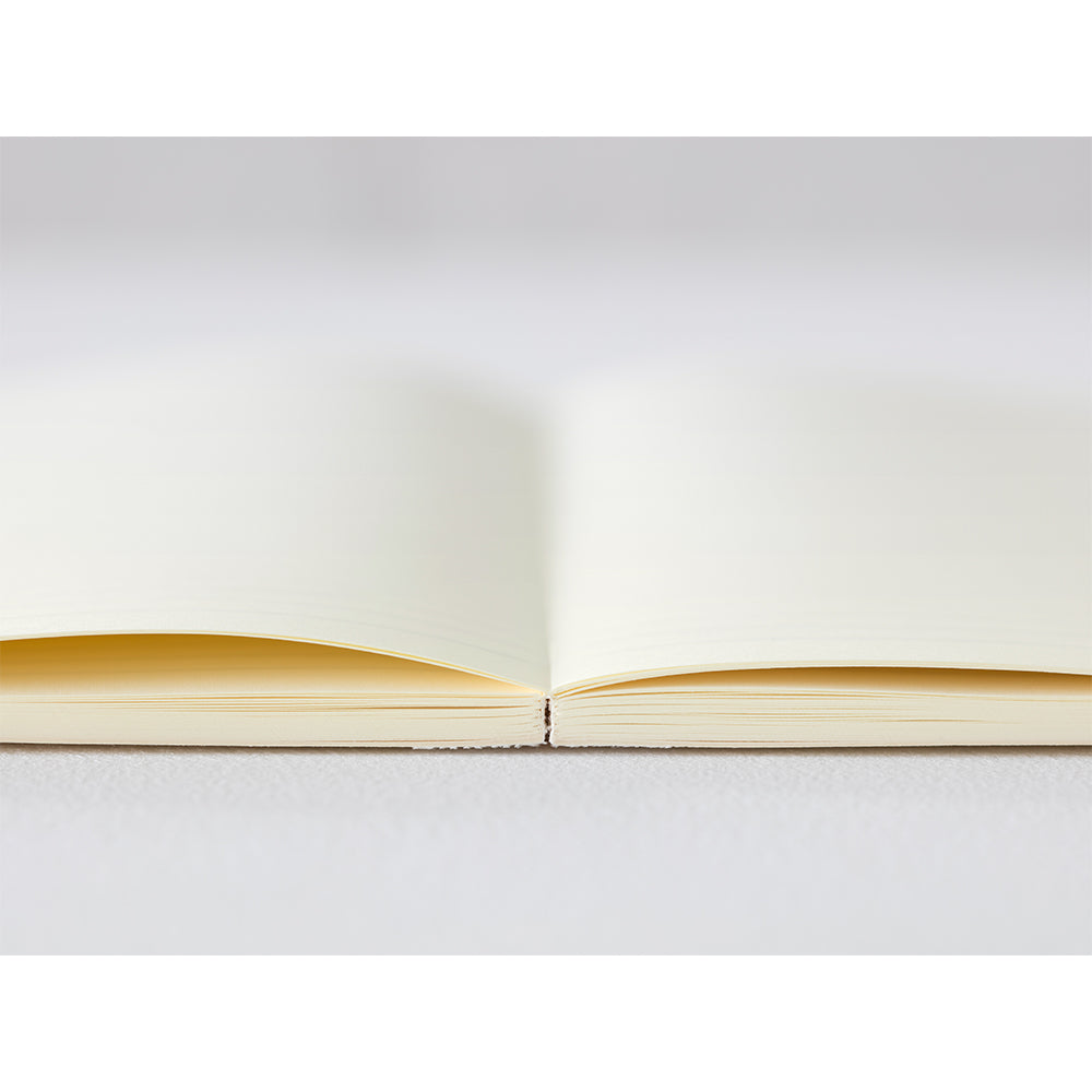 A5 MD Notebook Diary 2026 with a minimalist cream-toned glassine paper cover, thread-stitched binding, and a white bookmark string. The open spread displays a block-style monthly calendar on one side and lined memo pages on the other, printed on smooth MD PAPER designed for a premium writing experience.