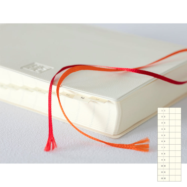 MD Notebook Diary (A6) 1 Day 1 Page 2026 with a minimalist PVC cover, featuring a year stamp on the spine, two bookmark strings, and monthly index tabs. The diary is open to reveal its premium MD PAPER with a clean, spacious layout for daily entries.