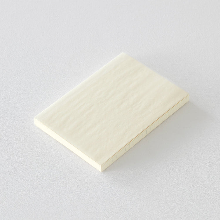A6 MD Notebook Diary 2026 with a minimalist cream glassine paper cover, featuring monthly block schedule pages, weekly planning sections divided into eight segments, and blank memo pages. Thread-bound for 180-degree flat opening, complete with a slim bookmark string and index label.