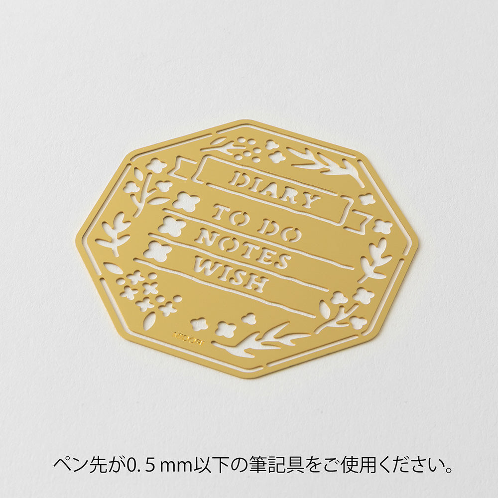 A brass stencil with floral and leafy cut-outs forming wreath-style designs, along with headings, to-do boxes, and animal details for decorating planners and memos.