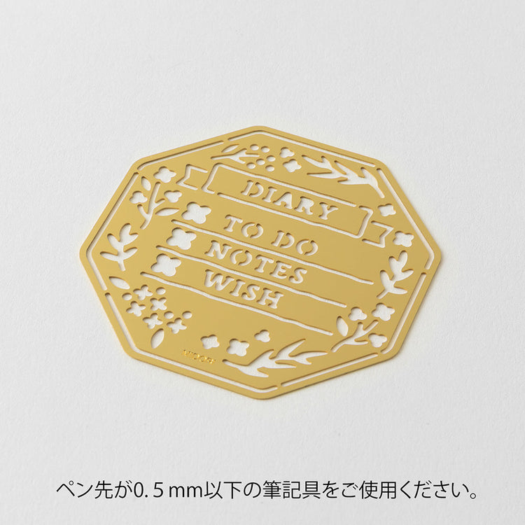 A brass stencil with floral and leafy cut-outs forming wreath-style designs, along with headings, to-do boxes, and animal details for decorating planners and memos.