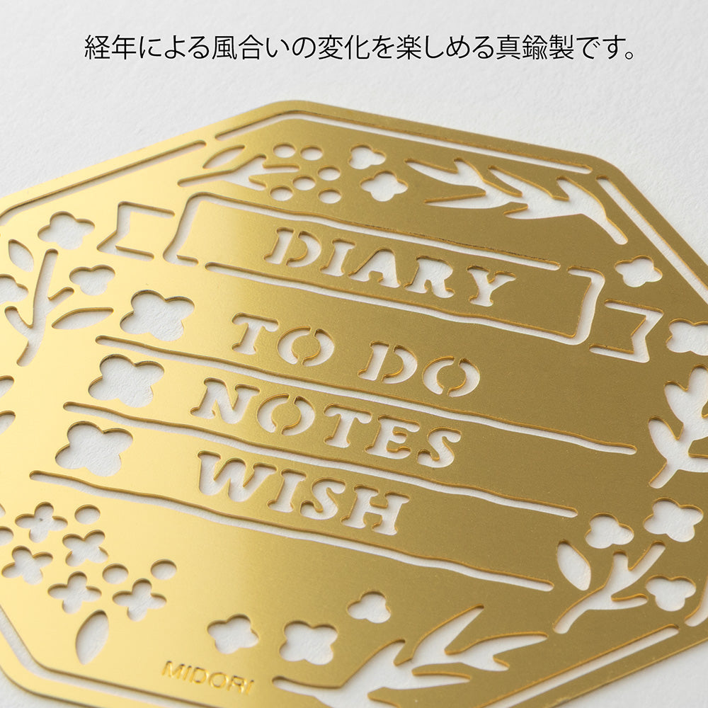 A brass stencil with floral and leafy cut-outs forming wreath-style designs, along with headings, to-do boxes, and animal details for decorating planners and memos.