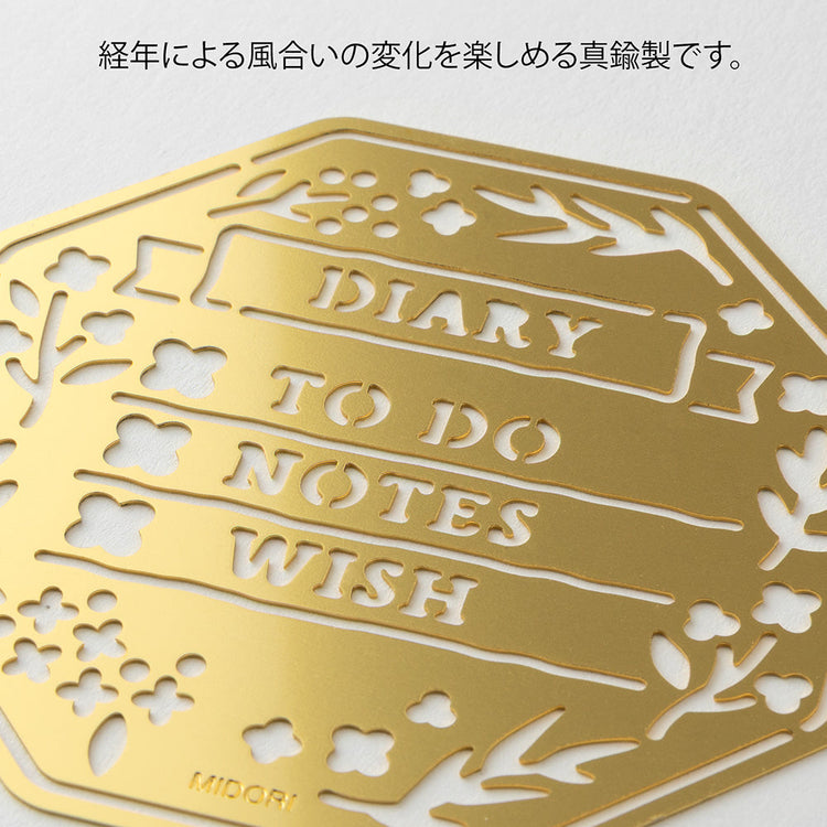 A brass stencil with floral and leafy cut-outs forming wreath-style designs, along with headings, to-do boxes, and animal details for decorating planners and memos.