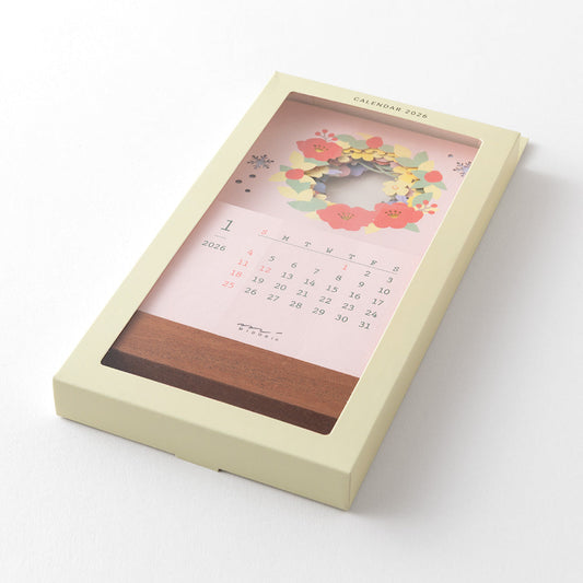 A delicate 2026 desktop calendar featuring layered, laser-cut floral designs that change with the seasons. Each month reveals a new arrangement of blossoms, displayed on a compact wooden stand, bringing an artful and elegant touch to any desk or small space.