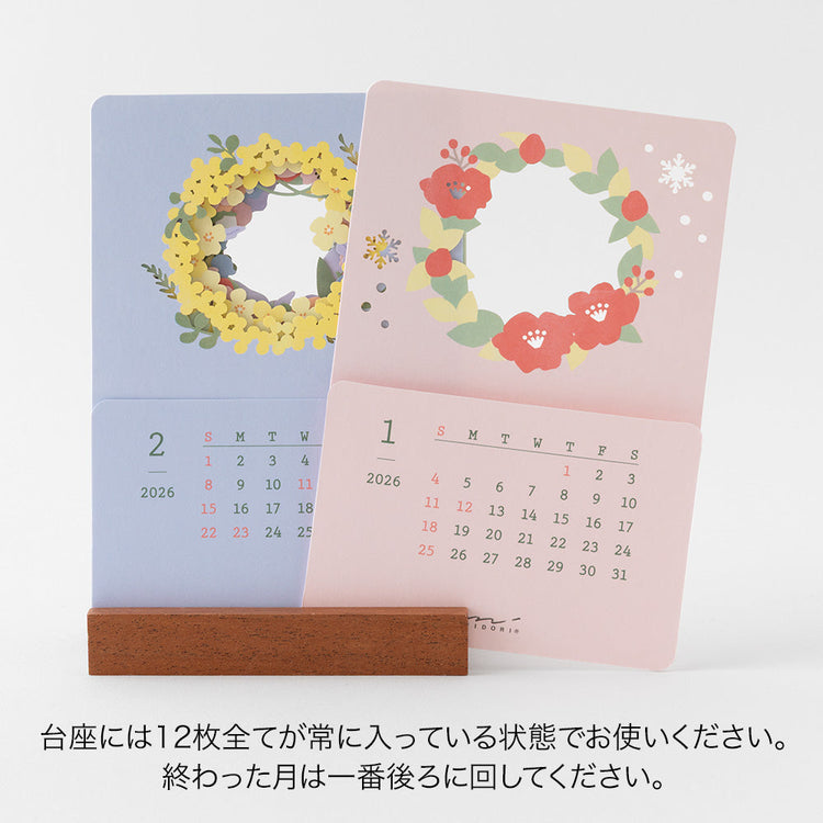 A delicate 2026 desktop calendar featuring layered, laser-cut floral designs that change with the seasons. Each month reveals a new arrangement of blossoms, displayed on a compact wooden stand, bringing an artful and elegant touch to any desk or small space.