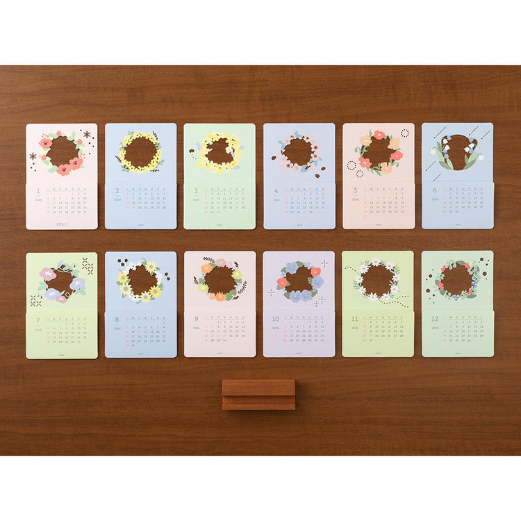 A delicate 2026 desktop calendar featuring layered, laser-cut floral designs that change with the seasons. Each month reveals a new arrangement of blossoms, displayed on a compact wooden stand, bringing an artful and elegant touch to any desk or small space.