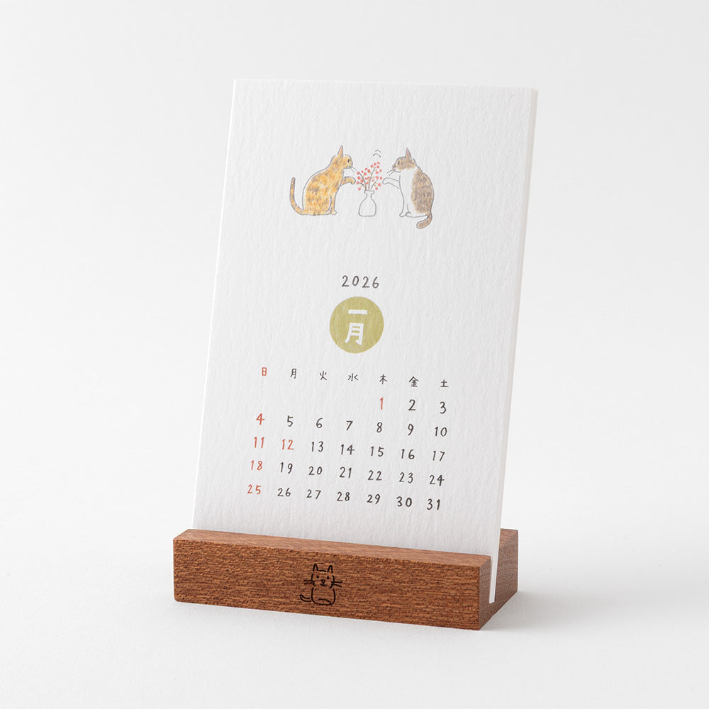 Midori Stand Calendar 2026 – Cat, a slim desktop calendar with a wooden stand, featuring soft, hand-drawn illustrations of cats by Sayo Koizumi in seasonal scenes.