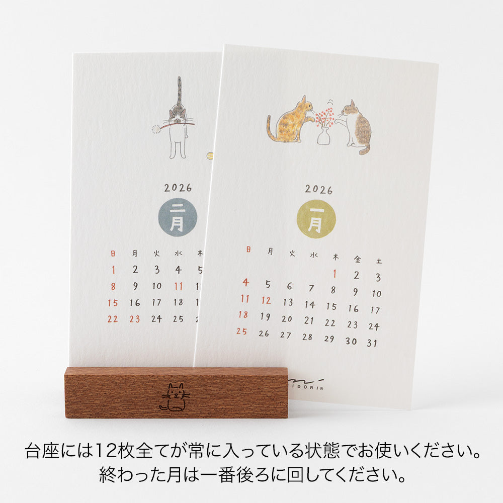 Midori Stand Calendar 2026 – Cat, a slim desktop calendar with a wooden stand, featuring soft, hand-drawn illustrations of cats by Sayo Koizumi in seasonal scenes.