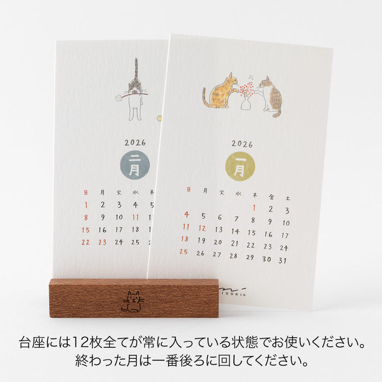 Midori Stand Calendar 2026 – Cat, a slim desktop calendar with a wooden stand, featuring soft, hand-drawn illustrations of cats by Sayo Koizumi in seasonal scenes.