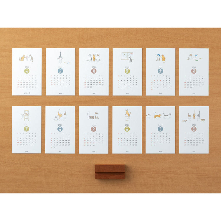 Midori Stand Calendar 2026 – Cat, a slim desktop calendar with a wooden stand, featuring soft, hand-drawn illustrations of cats by Sayo Koizumi in seasonal scenes.