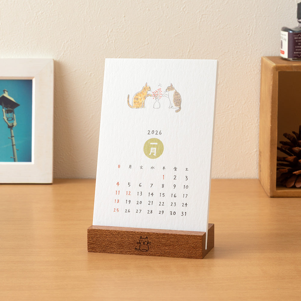Midori Stand Calendar 2026 – Cat, a slim desktop calendar with a wooden stand, featuring soft, hand-drawn illustrations of cats by Sayo Koizumi in seasonal scenes.